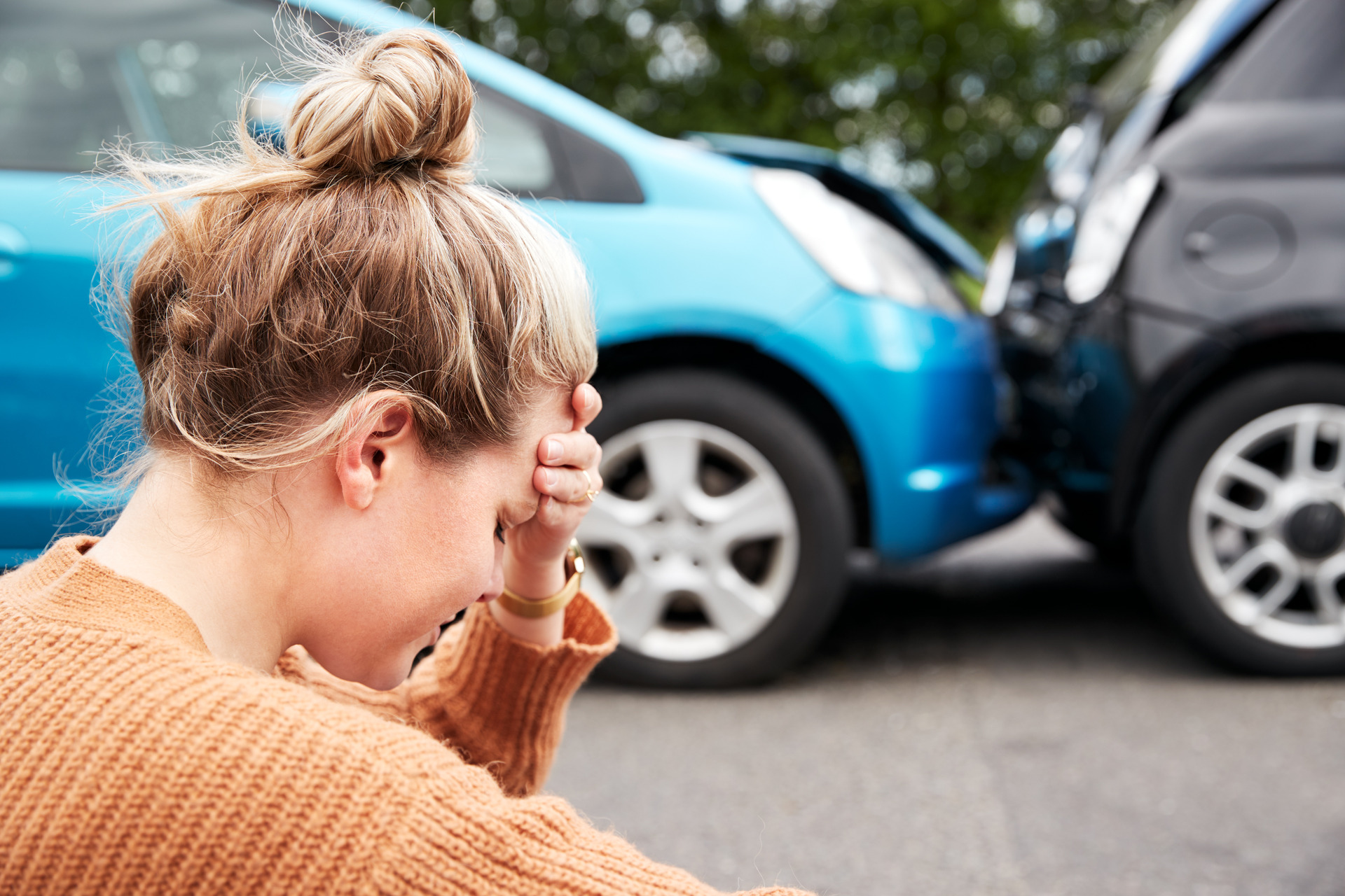 female driver with head in hands sitting next to a car crash