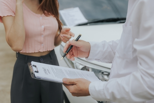 An insurance adjuster writing on a clipboard while speaking with a driver beside a damaged vehicle, illustrating claim evaluations often guided by a Savannah car accident lawyer.